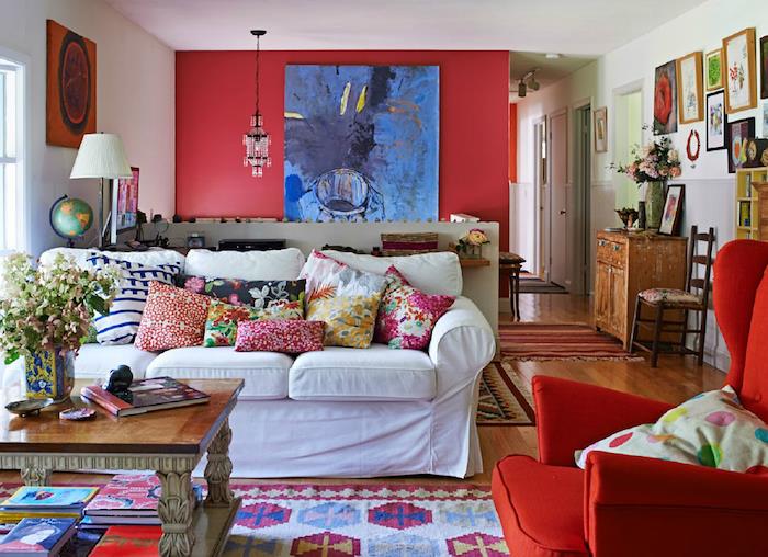 rdeča barva na naglasni steni, beli kavč, rdeč naslanjač, ​​pisane blazine in preproge, cvetlični vzorci, okvir za steno