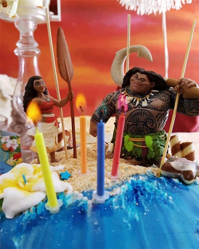 „Disney“ teminio pyrago dekoravimo idėja su Vaianos ir Maui personažų figūromis ant sutrupinto sausainių smėlio sluoksnio