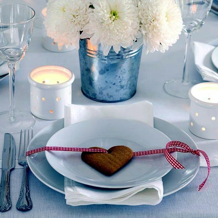 širdies formos sausainis, dvi baltos lėkštės, du žvakidės, antspaudas baltomis gėlėmis, vyno taurės