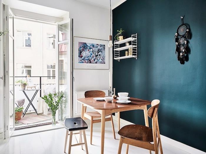 valgomojo dekoras su naftos sienos dalimi, tamsiai mėlynas atspalvis, medinis stalas ir kėdės, baltos grindys, juodos svajonių gaudyklės sienų dekoras