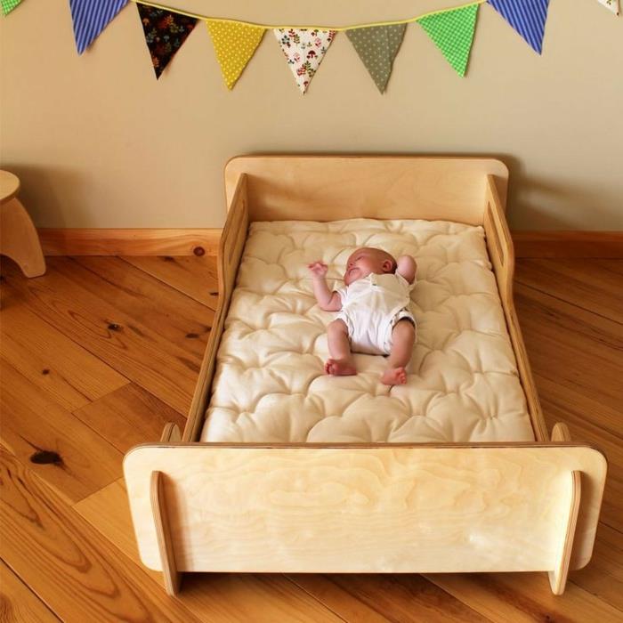 montessori yatak odası, montessori yatak mobilyaları, yatağın üstünde renkli duvar dekorasyonu, sessiz bir atmosfer, yatakta mutlu bebek