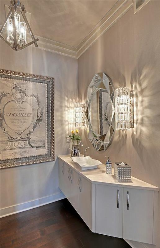 mažas vonios kambarys su liustra ir krištoline sienine lempa su balta pakabinama spintele