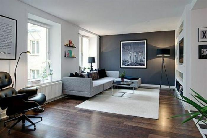 dažų spalvos svetainė, baltas kilimas, tamsios medinės grindys, pasukama kėdė, didelė pilka sofa, kurią sieną dažyti tamsia spalva