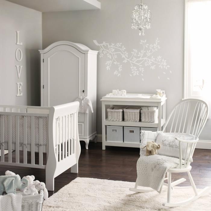 balta kūdikio lova, kėdė, baltas kilimas ir drabužių spinta, minkšta ir raminanti atmosfera berniuko kambaryje