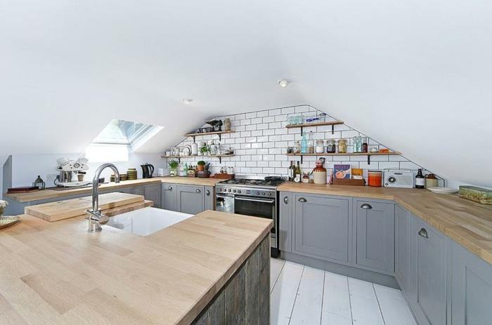 maža virtuvė su nuožulniomis lubomis, medinė virtuvės sala, baltos lentos, metro plytos, pilkos ir medinės spintelės