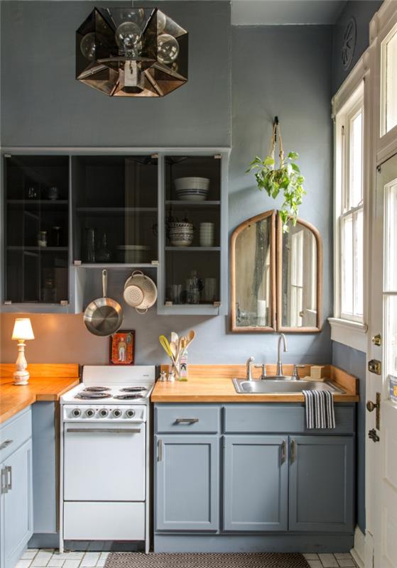 mėlyna virtuvė, 6m2 virtuvė, šviesiai mėlynos spintelės, maža senovinė viryklė, stiklinė indauja, dekoratyvinis veidrodis