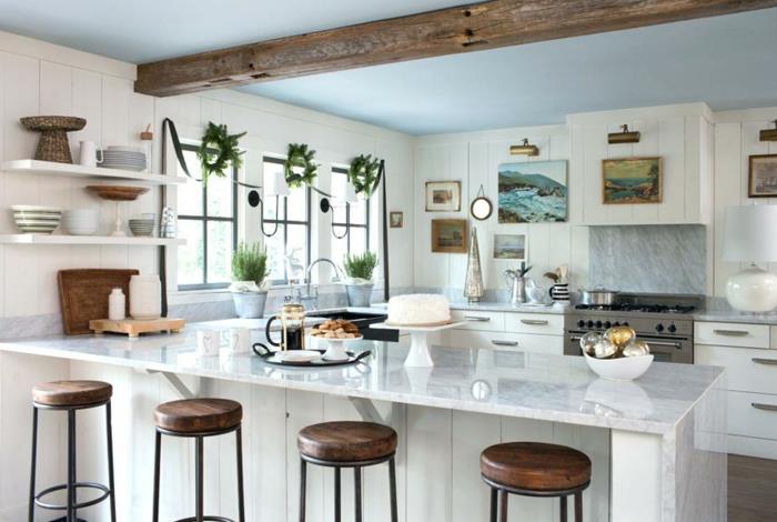 stilinga balta ir medinė virtuvė, medinė sija ant lubų, medinės ir metalinės kėdės, šviesiai mėlynos lubos, baltos lentynos