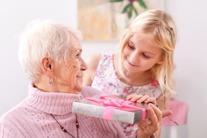Babičin dan DIY, lepa embalaža s srebrnim papirjem in rožnatim trakom, vnukinja z blond lasmi in njena babica z belimi lasmi