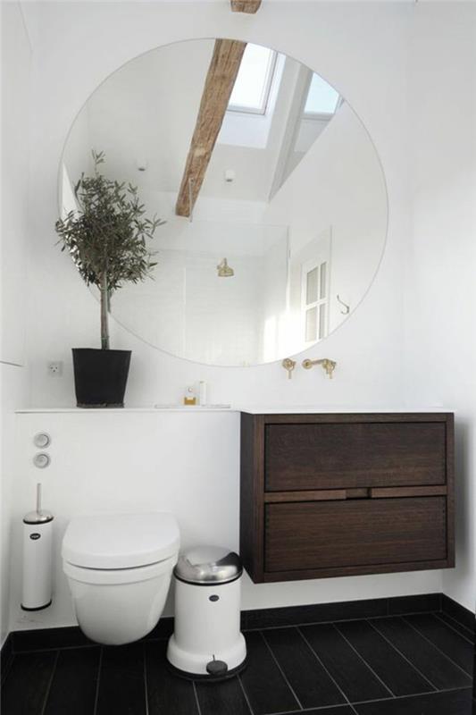 labai mažas vonios kambarys su labai dideliu apvaliu veidrodžiu baltos sienos ruda pakabinama spintelė