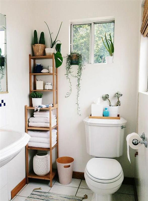 vonios kambarys, drėgmę sugeriantis augalas, kambarinis augalas, nukritęs augalas, etninio stiliaus lentyna, baltos plytelės, klasikinė balta tualeto spintelė, žali augalai, organizuojami šalia mažo kvadratinio lango