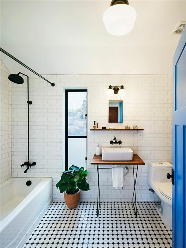 mažas vonios kambarys su vonia ir baltomis plytomis su giliai mėlynomis durimis