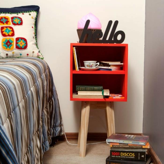 mažas raudonas naktinis stalas su medinėmis kojelėmis, kratinė pagalvėlė su labai spalvingais raštais