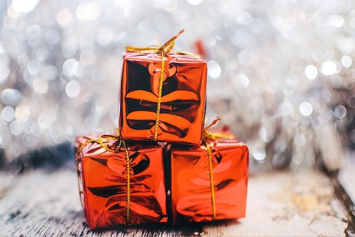 mažos dovanos raudona pakuotė su auksine virvele baltame fone, sidabrinė girlianda ant medinio stalo, paprastas kalėdinis fonas