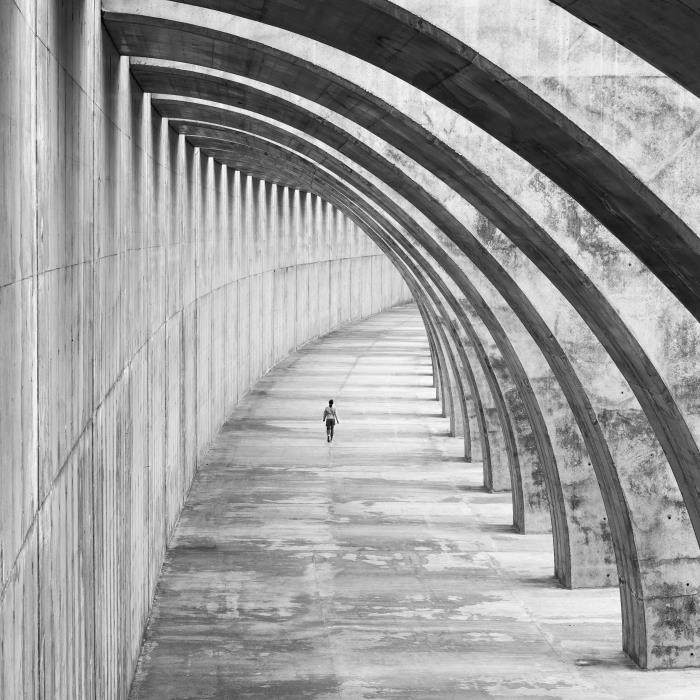 črno -bela fotografija ženske, ki hodi pod betonskim lokom, izvirna fotografija sodobne stavbe