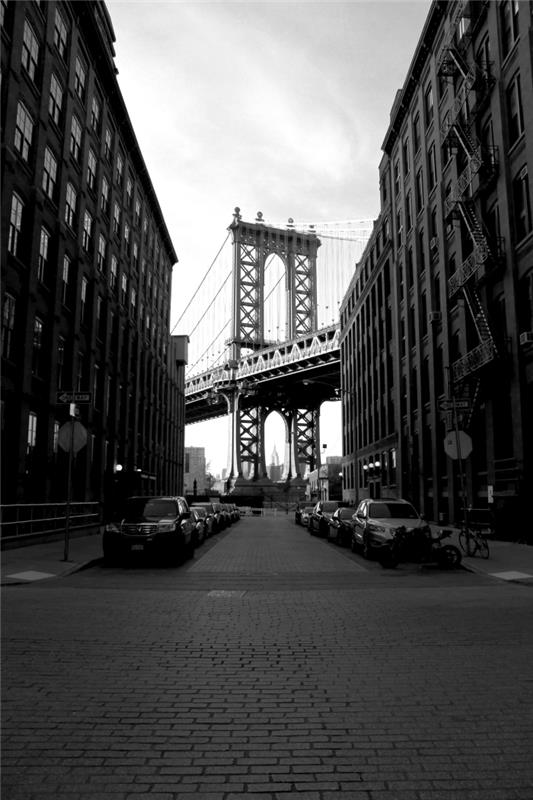 pogled na del newyorškega mostu med visokimi zgradbami, črno -belo mestno pokrajino iz prvotne perspektive