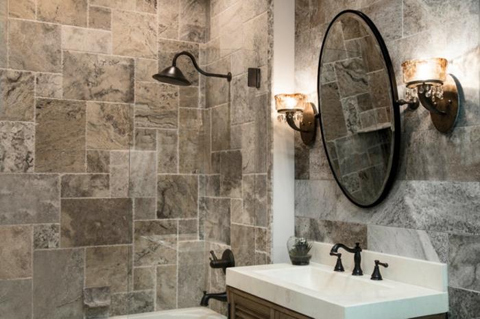 yuvarlak duvar aynası, beyaz lavabo, iki duvar lambası, küçük duş alanı, traverten taşı