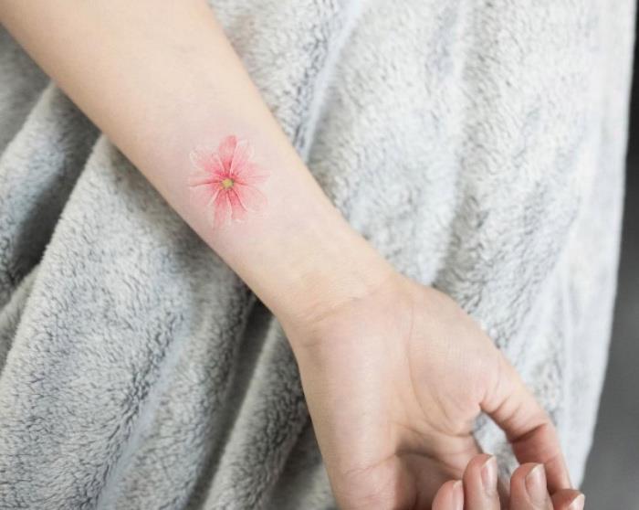 rožinė riešo tatuiruotė, mažos drugelio tatuiruotės, ranka priešais pilką kailio antklodę