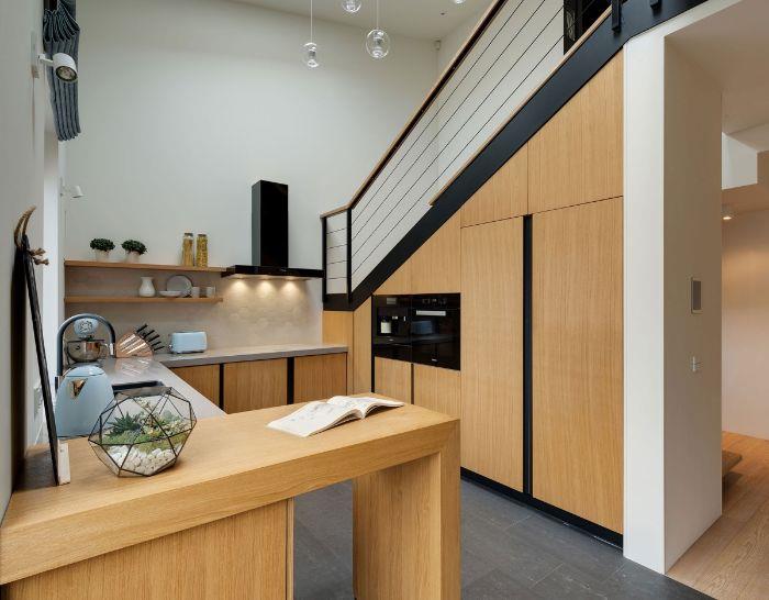 kuhinjske omare pod stopnicami lesena kuhinja in siva talna obloga bele delovne plošče odprte police