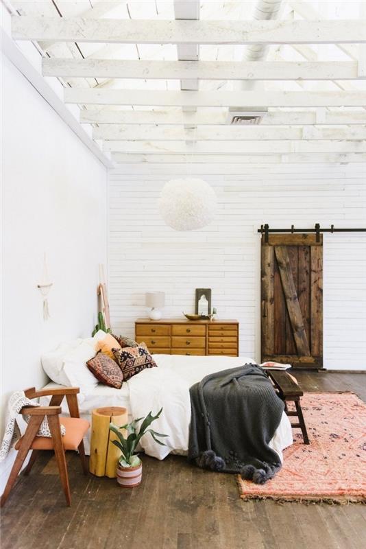 Bohemijos stiliaus miegamojo dizaino idėja su mediniais baldais, kambarys su aukštomis lubomis su baltomis medinėmis sijomis