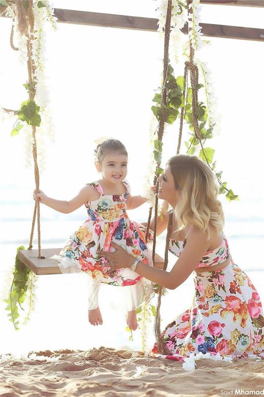 Paplūdimio nuotraukos motinos dukros suknelės iš to paties audinio ir to paties gėlių rašto, bet skirtingų modelių, mamos ir dukros aprangos idėja, motinos dukros drabužiai