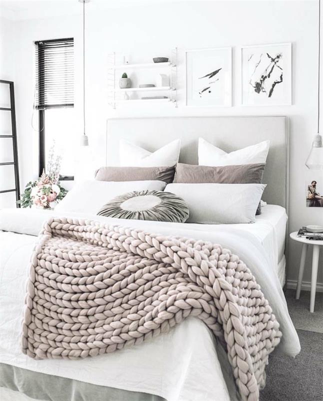 Skandinaviška dekoratyvinė lova, nuoga rožinė megzta pledas, pagalvėlės, paveikslai, maža balta taburetė