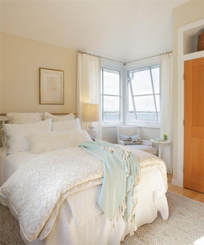 Deniz manzaralı yatak odası düzeni, bej ve beyaz minderlerle kaplı geniş yatak ve rahatlatıcı bir atmosfer için ekose, beyaz ve bej dekor