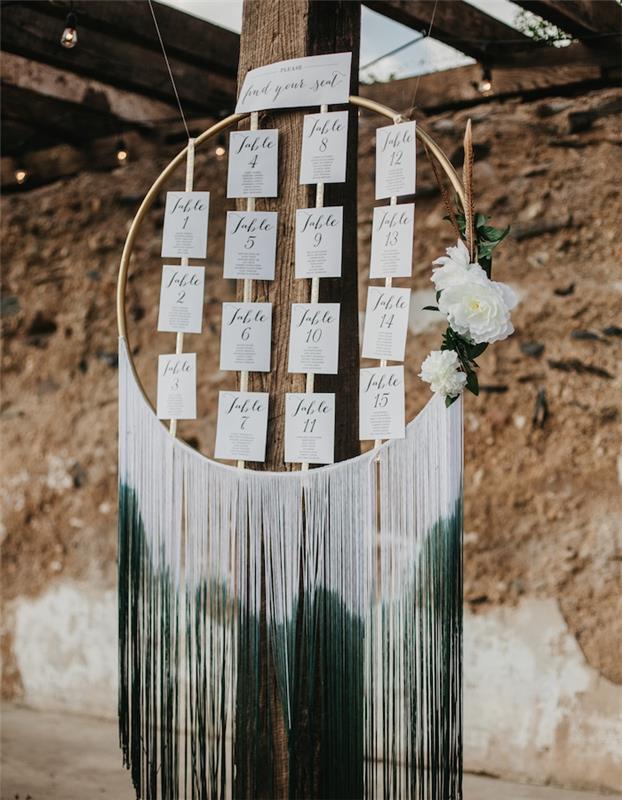 vestuvių stalo planas mediniame lanke, baltos svečio vardo etiketės ir balta ir žalia ombré macrame, baltų gėlių puošmena