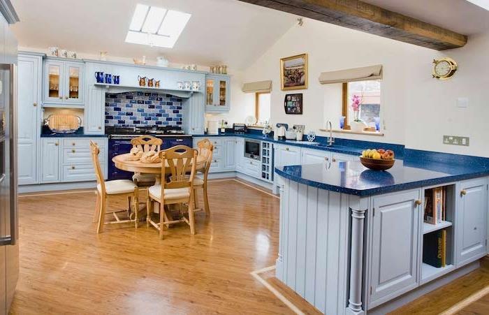 nebesno modra kuhinjska omara in temno modra delovna plošča, parket iz svetlega lesa, izpostavljen žarek, modra ploščica