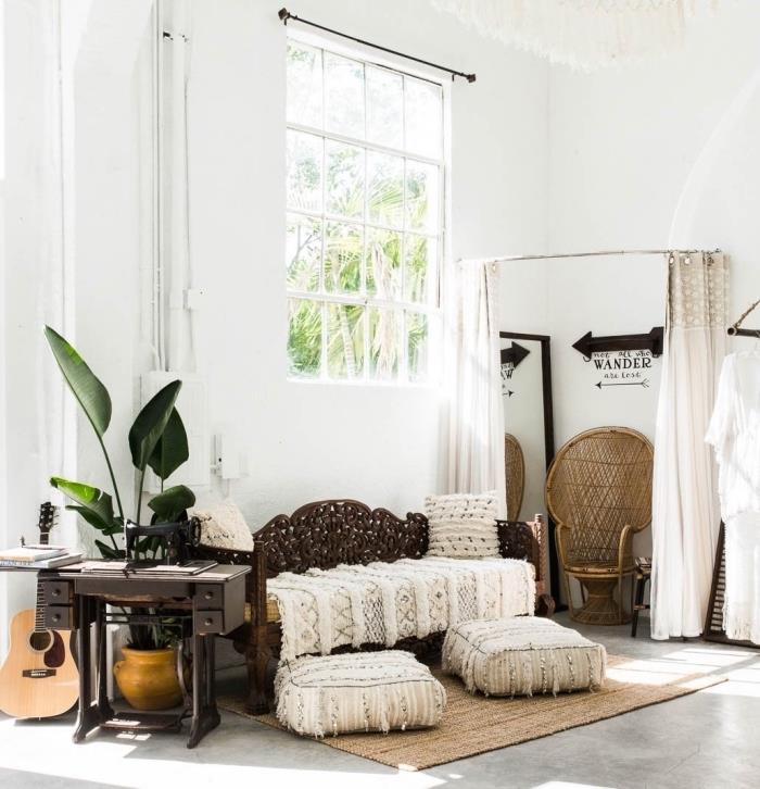 elegantiško bohemiško stiliaus kambarys su baltomis sienomis ir betoninio dizaino grindimis, padengtomis smėlio spalvos kilimu ir berberinėmis pagalvėmis