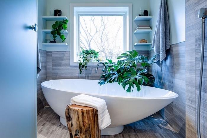 Zen vzdušje v kopalnici z zelenimi rastlinami, navpično shranjevanje belega pobarvanega lesa, beli samostoječi model kadi