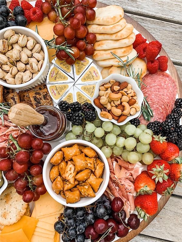 apero krožnik z narezki siri sadje in oreški na okroglem lesenem krožniku