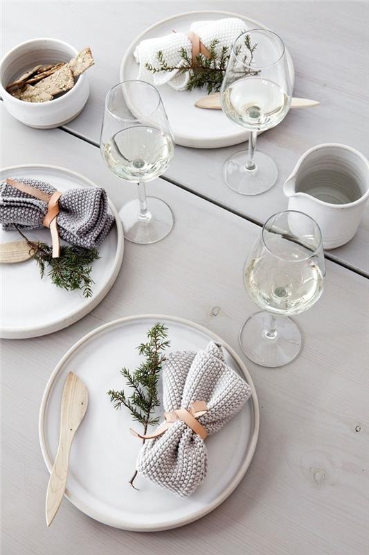 ideja zlaganja belih prtičkov Božični dekor v minimalističnem slogu bela lesena miza bela okrogla plošča jelkova vejica