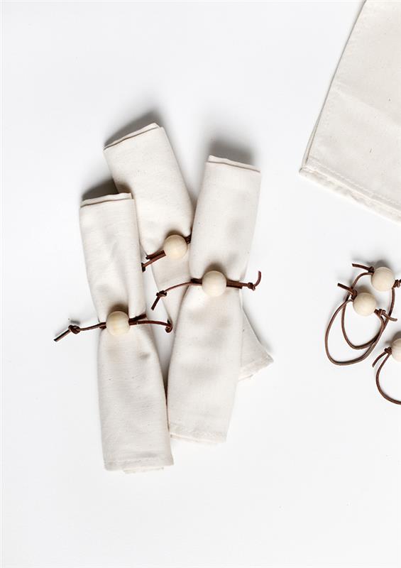 sulankstomos vienos servetėlės, baltos servetėlės ​​suvyniotos su servetėlių laikikliu rudose odinėse juostose su baltu rutuliu