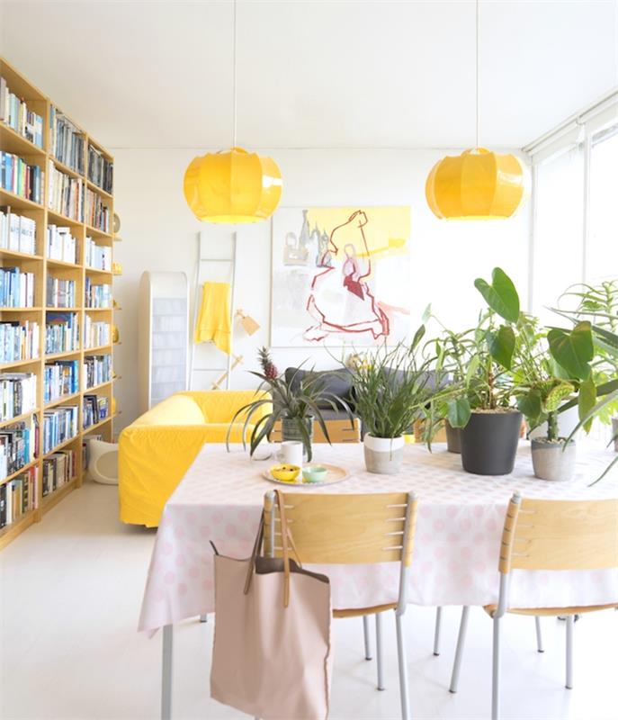 beli dekor dnevne sobe z rumenimi in zelenimi poudarki, lončki za rastline na mizi za jasle, lesena knjižna polica, bele stene