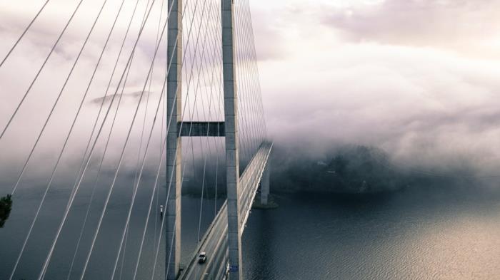 rūke pasimetusio tilto vaizdas, paslaptingo rojaus kraštovaizdžio efektas, tiltu važiuojantys automobiliai, šiek tiek susijaudinęs vanduo