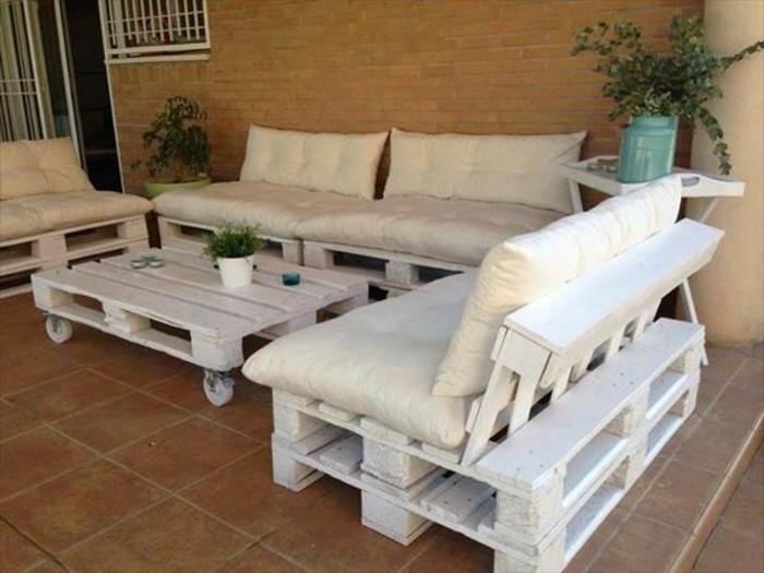trijų baltų sofų komplektas, pagamintas iš padėklų, padengtų pagalvėmis, ir atitinkamas baltas padėklų stalas ant ratų, kaip pagaminti padėklų baldus, pastatytas ant verandos