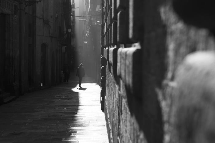 črno -bela fotografija uličnega moškega, ki hodi po ozki uličici, in svetloba, ki pada na del pločnika