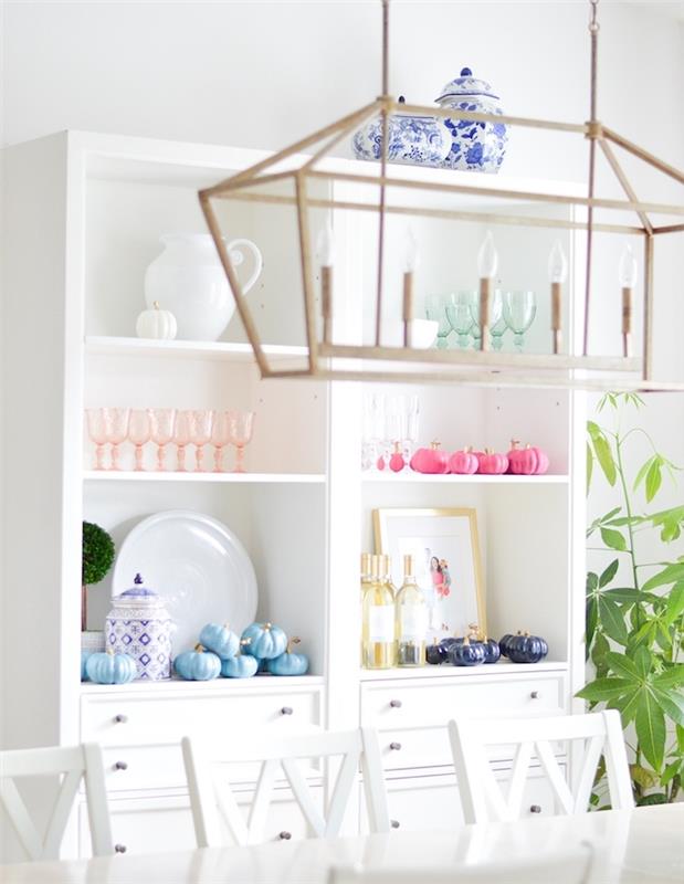 okras z bučami buče prebarvane v vijolično, modro in rožnato barvo na belem omarici, beli mizi in stolu