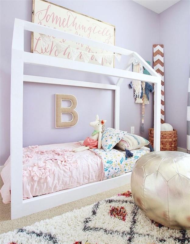 violetinės sienos ir balta lova su maža lova su spalvota patalyne, juodai baltas kilimas, vaikiškas pufas, austas žaislų krepšelis