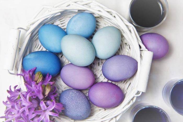 beyaza boyanmış bitkisel lif sepetine yerleştirilmiş mavi ve mor tonlarında yenilebilir boyayla boyanmış paskalya yumurtası örnekleri