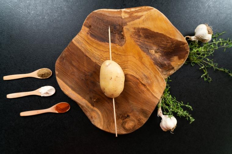 Krompir a ventaglio, patata con la buccia so uno spiedino di legno, cucchiai di legno con spezie