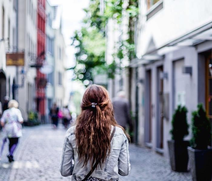 pričeska v ležernem slogu s kodri in na pol privezanimi dodatki za lase, obleka v jeans jakni in belo -črni bluzi