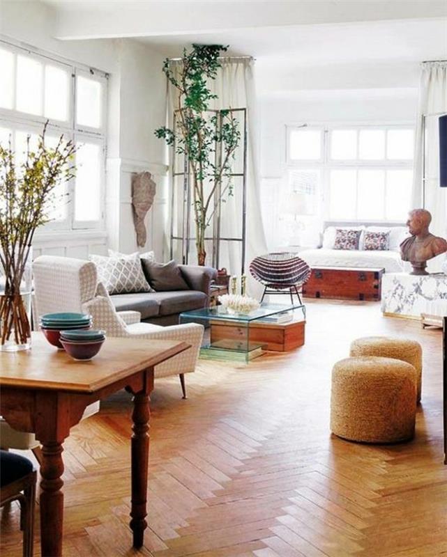 un pavimento v parketu, tavolo in legno, un divano grigio, piante e oggetti d'arte per arredare monolocale