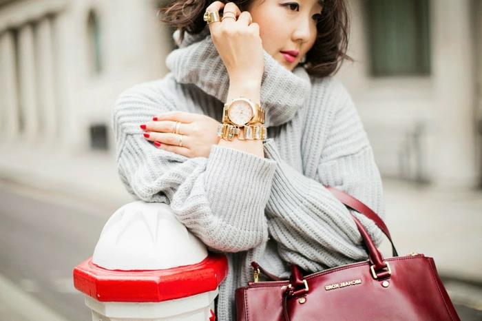 pilkas megztinis ir bordo spalvos krepšys, laisvas moteriškas megztinis, auksinis laikrodis, metalinė apyrankė, raudonas nagų lakas, prašmatni moters apranga
