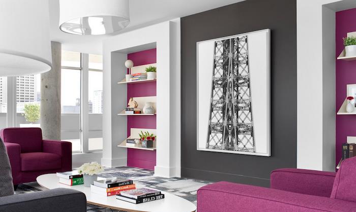 violetinės ir tamsiai pilkos detalės ant baltų sienų, didelėje svetainėje, su dviem purpuriniais foteliais, spalvomis, derančiomis prie pilkų sienų, baltu ovaliu kavos staliuku, keliomis knygomis ir gėlėmis