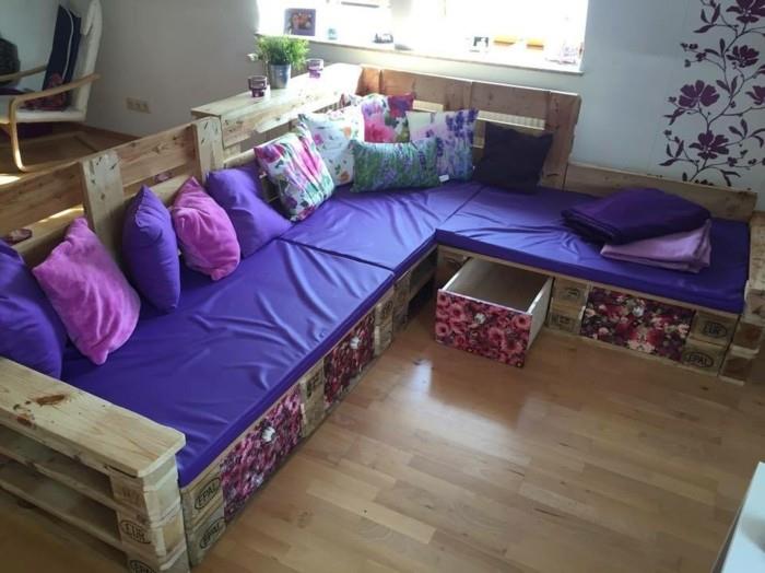 violetinės ir violetinės spalvos užvalkalai ir pagalvės, ant pasidaryk pats sofos, pagamintos iš medinių padėklų, su sandėliavimo vietomis, keliomis įvairiaspalvėmis pagalvėlėmis