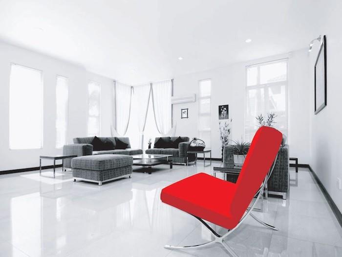 modernus svetainės modelis, kurio spalva derės prie pilkų, baltų sienų, grindų ir lubų, pilka sofa ir išmatos, juodos dekoratyvinės pagalvėlės, raudonas fermas