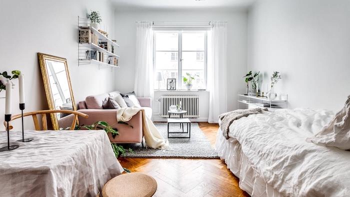 Šiaurietiškas dekoras dizainerio miegamajame su rožine sofa, balta lova, viengubu stalu, medinėmis grindimis, knygų lentyna