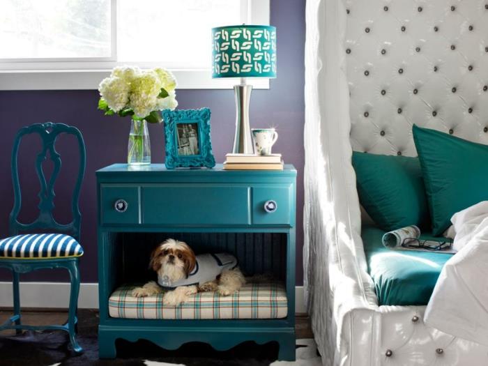 didelė pilka sofa -lova, mėlynas naktinis stalas su dviem stalčiais, barokinė kėdė turkio spalvos naktinėje lempoje