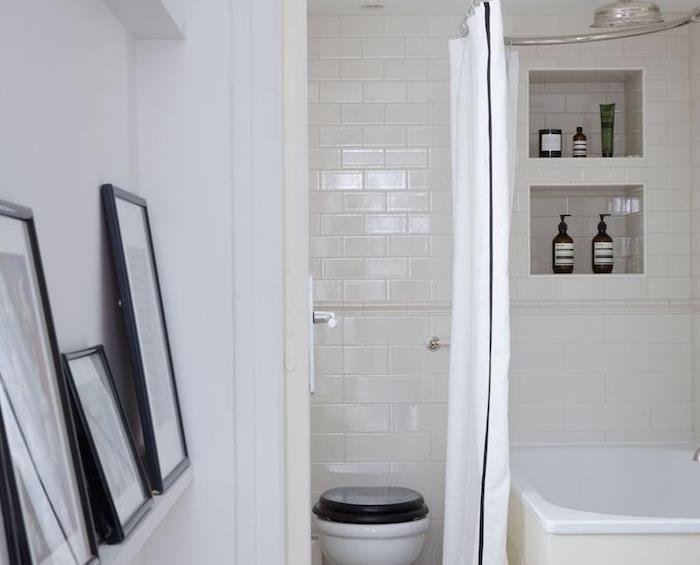 beyaz küvet, duvar depolama nişi, siyah beyaz tuvalet ve grafik çerçeve dekorlu küçük beyaz banyo dekorasyonu